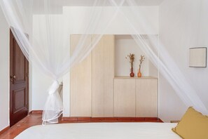 A bedroom with a bed, a bedside table with two vases, a wardrobe, and a door with a curtain.