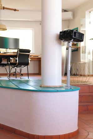 A corner of a room with a white pillar, a projector mounted on a stand, a table with chairs, and a window in the background. - House A: 4 Suites |Pool Garden Sauna Tennis (Seixal)
