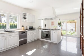 A modern kitchen with white cabinetry, stainless steel appliances, and a large window overlooking a garden. - House A: 4 Suites |Pool Garden Sauna Tennis (Seixal)