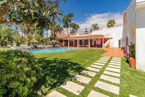 A pool area with a clear sky, a well-maintained lawn, and a building with a red-tiled roof.
