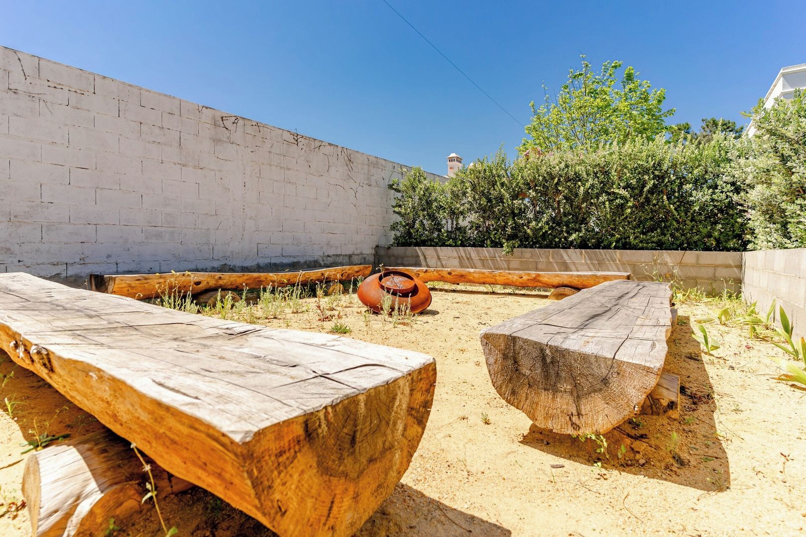 A sandy outdoor area with wooden benches and a large pot.