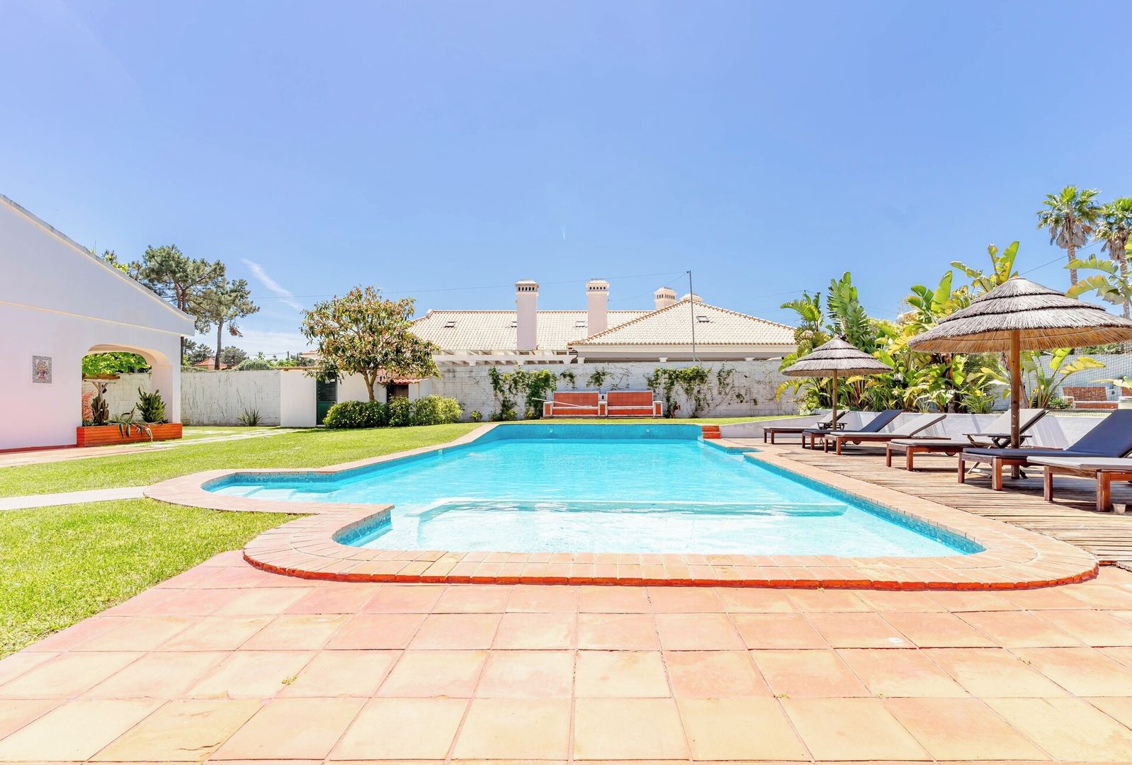 A swimming pool with a tiled deck, lounge chairs, and a building in the background.