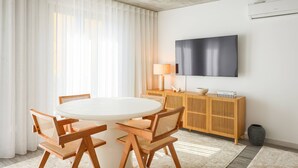 Uma área de jantar moderna com mesa redonda, cadeiras de madeira, televisão na parede e um console de madeira com abajur.
