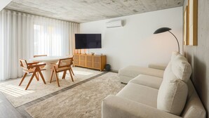 Uma sala de estar moderna com uma mesa de jantar redonda, cadeiras de madeira, um sofá bege, uma televisão de tela plana e um design minimalista.