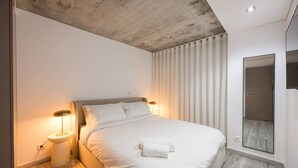 Quarto moderno com uma cama grande, duas luminárias de cabeceira, um espelho e teto de madeira.