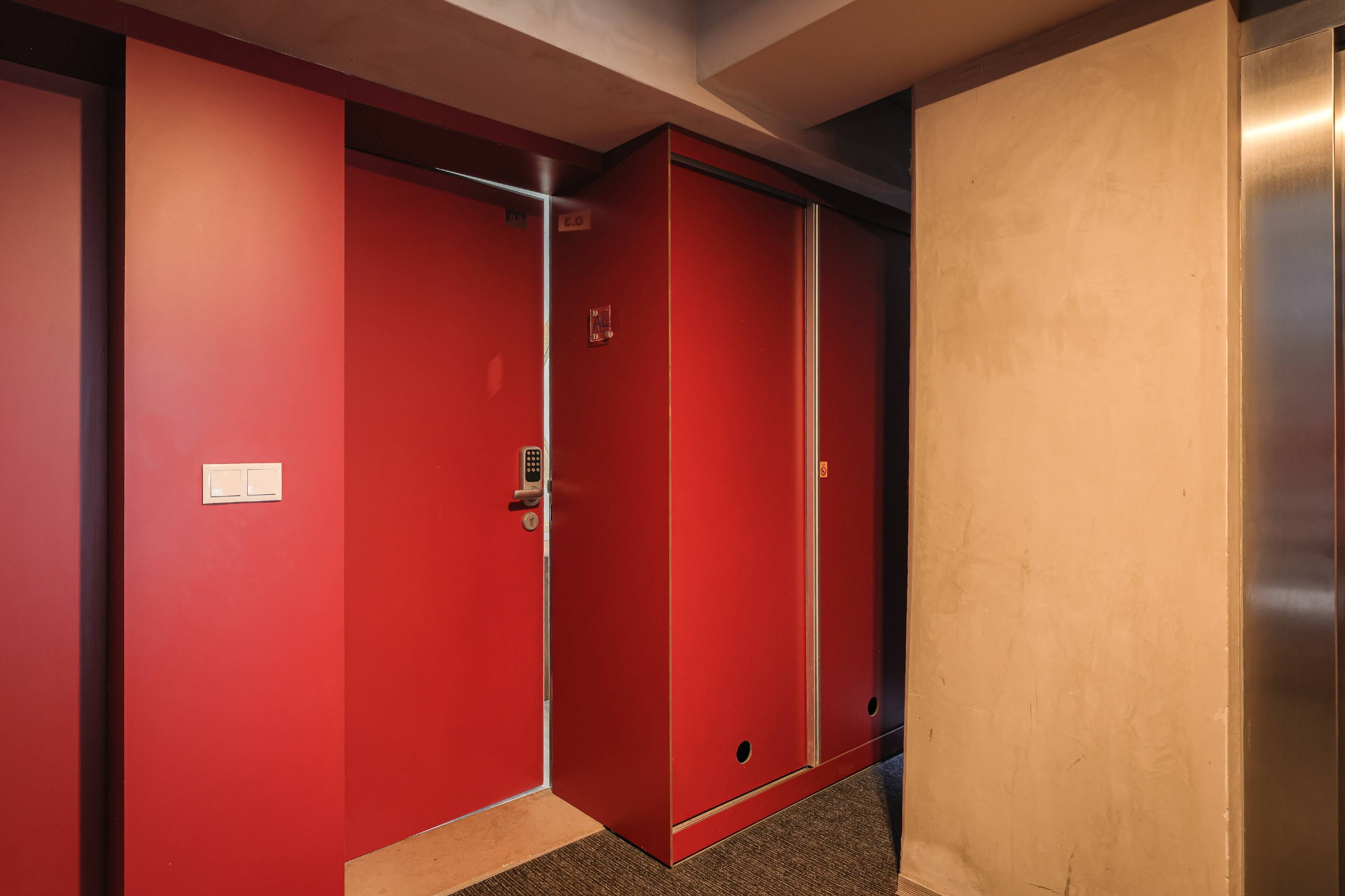 A red elevator with a keypad lock and a light switch on the wall.