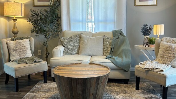 Una sala de estar con un sofá, dos sillones, una mesa de centro y un ventanal con cortinas.