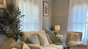Una sala de estar con un sofá color beige, un sillón verde, una mesa de centro redonda de madera y una planta grande en maceta.