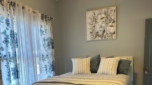 Un dormitorio con una cama, un banco, un ventilador de techo, un cuadro y una puerta.