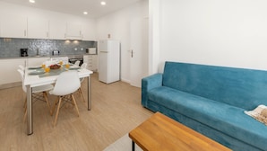 Une cuisine moderne avec des meubles blancs, une table à manger avec des chaises, un canapé bleu et une table basse en bois.