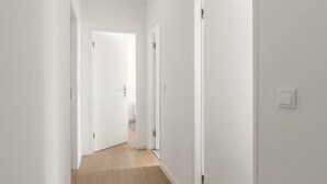 Un couloir étroit aux murs blancs et au plancher en bois, qui mène à plusieurs portes fermées.