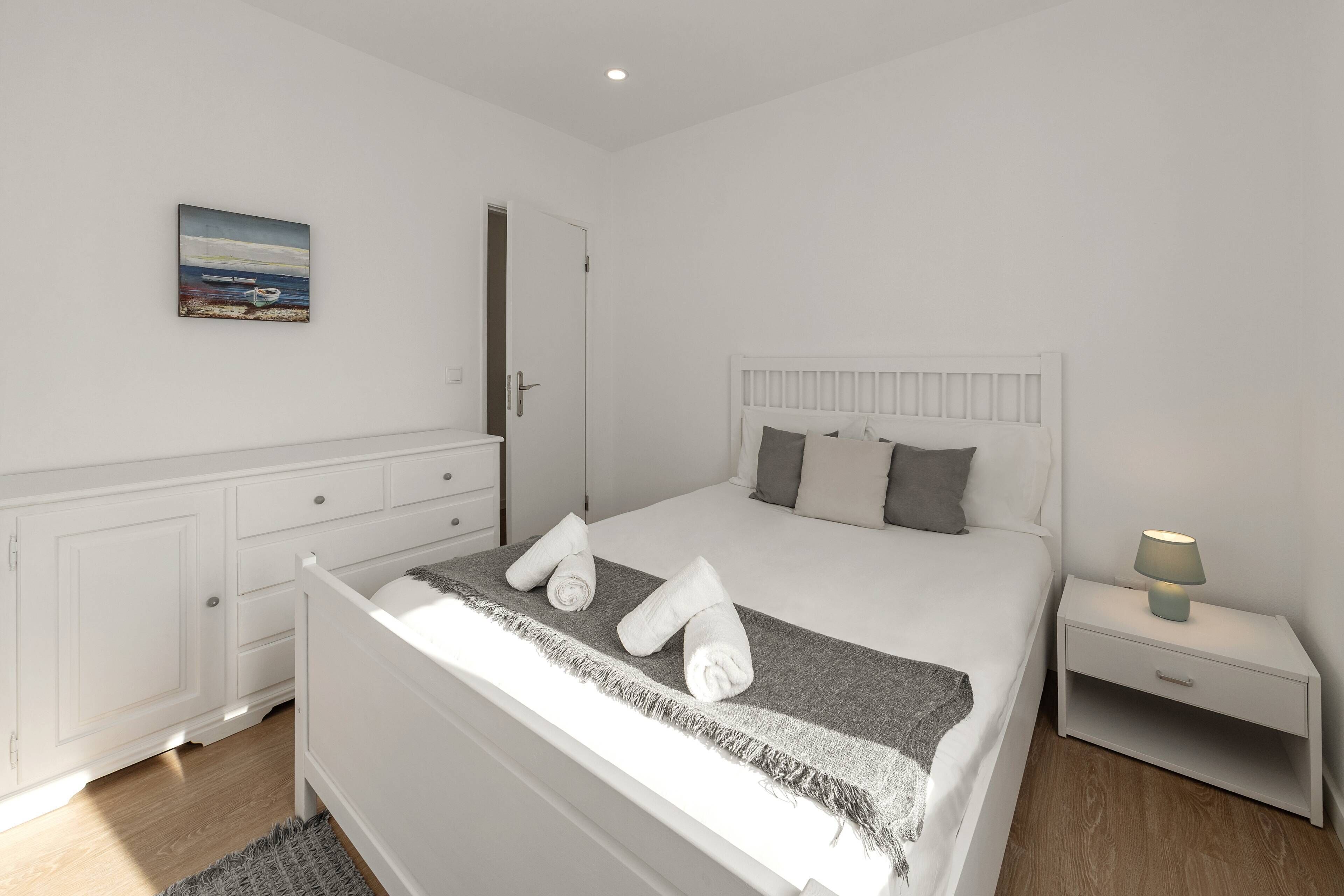 A neatly arranged bedroom with a bed, bedside table, and a painting on the wall.