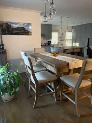 A modern kitchen with a central island, grey cabinets, pendant lighting, and a dining area with a wooden table and chairs.