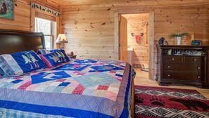 A cozy wooden cabin bedroom with a large bed, a dresser, a chandelier, and a door leading to another room. - Skyline Lodge, beautiful lodge home with mountain and lake view (Butler)