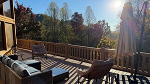 A wooden deck with outdoor furniture, including a sofa and chairs, overlooking a forested area. - Skyline Lodge, beautiful lodge home with mountain and lake view (Butler)