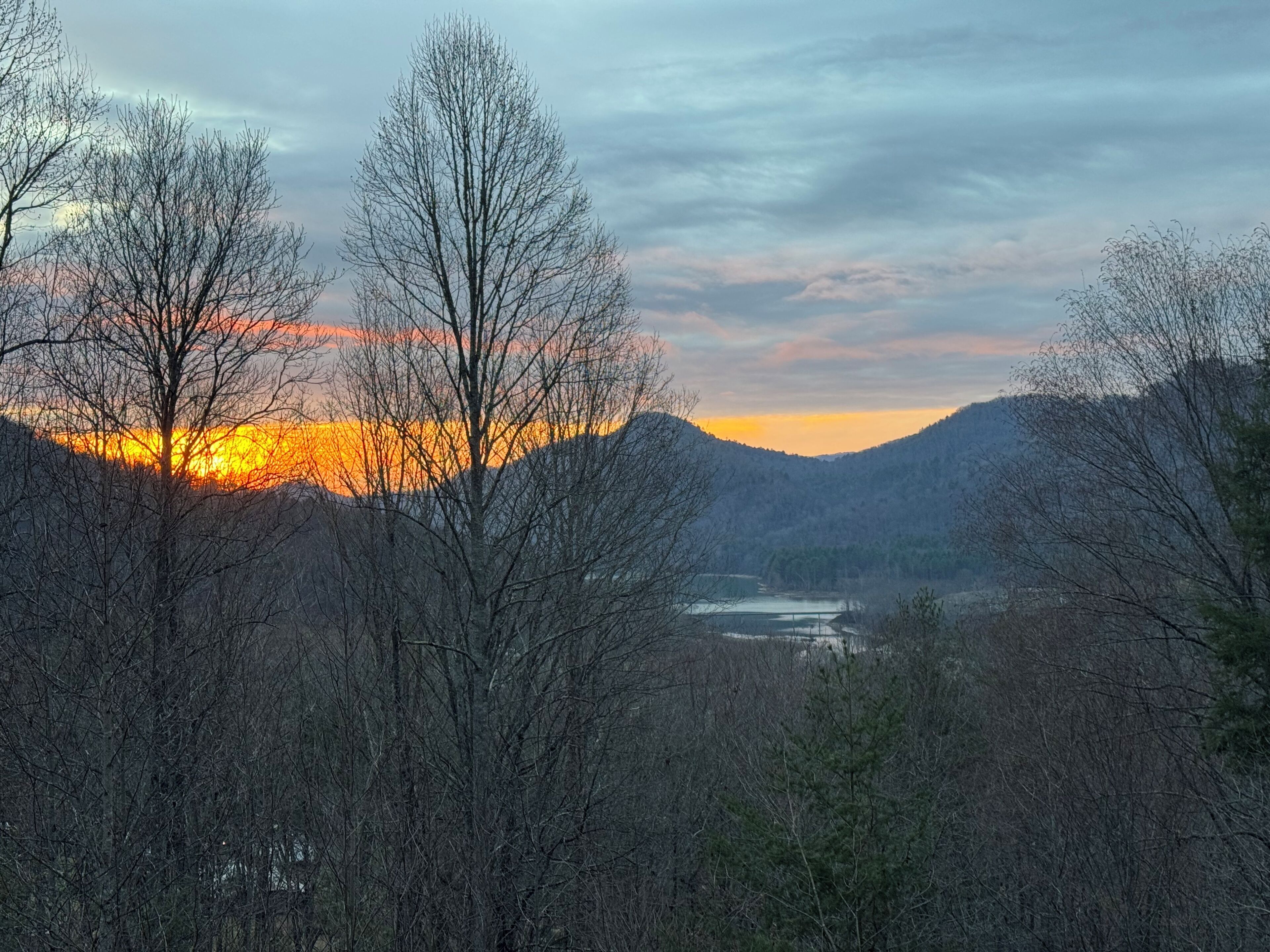 A mountainous landscape with a river and trees in the foreground.