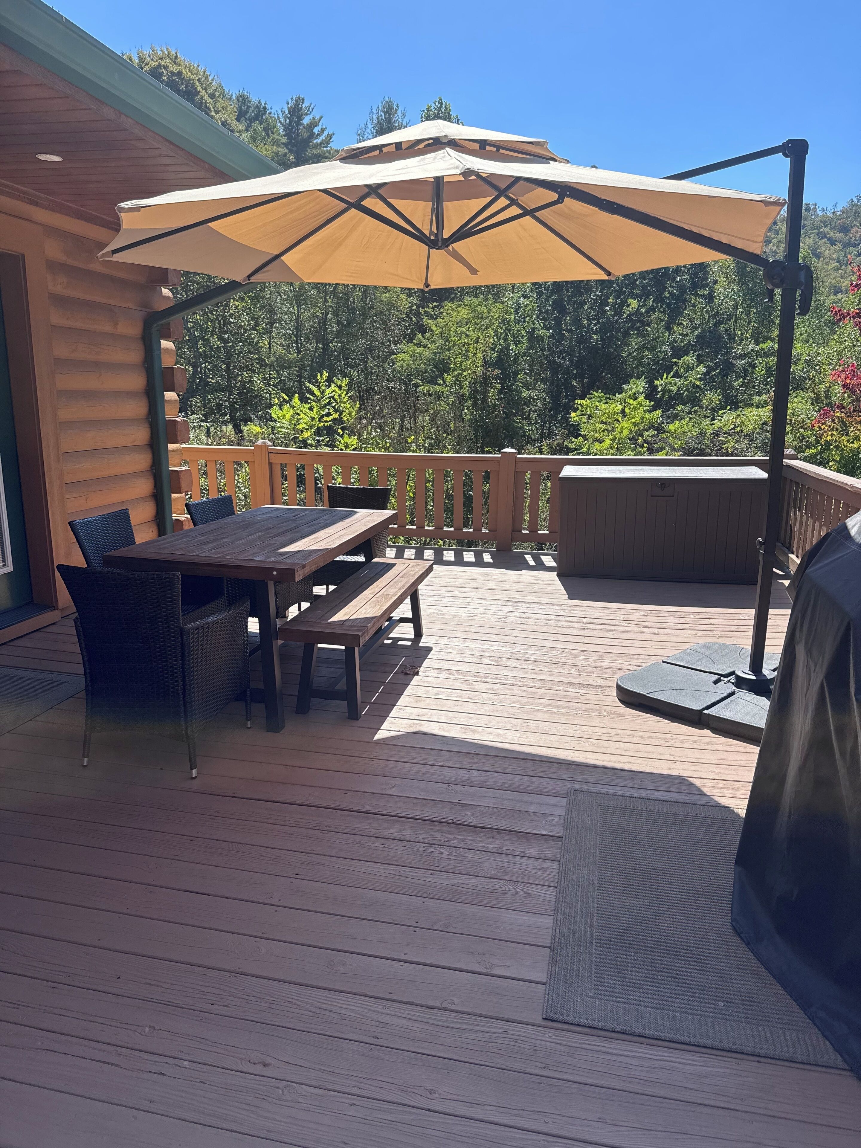 Un patio exterior con terraza de madera, una mesa con sillas, un paraguas grande y una parrilla.