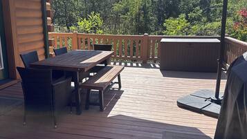 Un patio exterior con terraza de madera, una mesa con sillas, un paraguas grande y una parrilla.