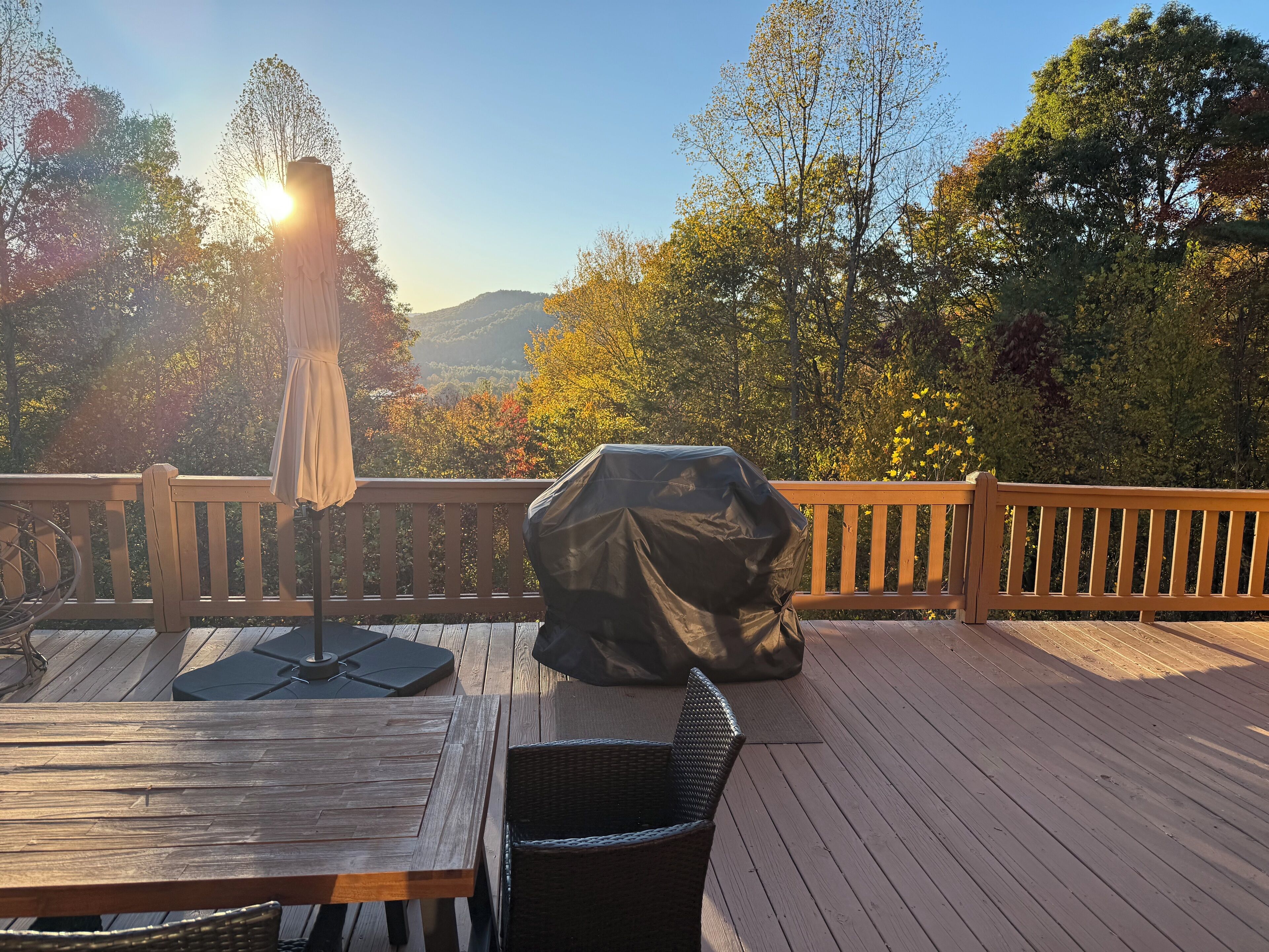 Una terraza de madera con una mesa, sillas, una parrilla cubierta y una sombrilla.