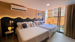 Camera d'albergo con due letti, un condizionatore, un comodino con lampada e vista all'esterno.