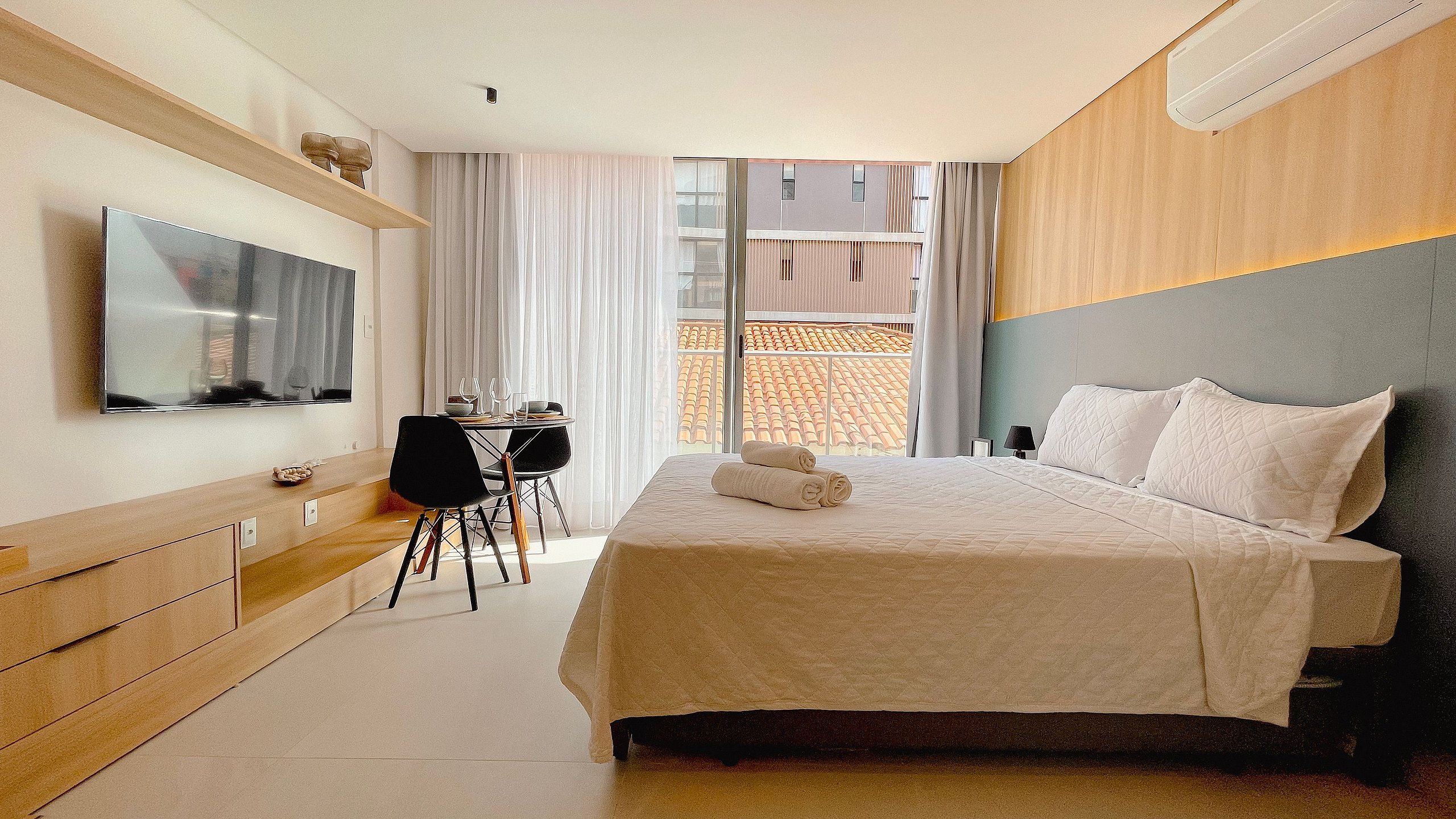A hotel room with a bed, a desk, a TV, and a window with a view of buildings.