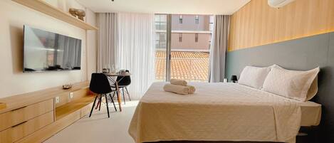 A hotel room with a bed, a desk, a TV, and a window with a view of buildings.