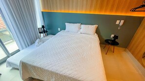 Ein Hotelzimmer mit einem großen Bett, einem Nachttisch mit Lampe, einem Sessel und Blick ins Freie.