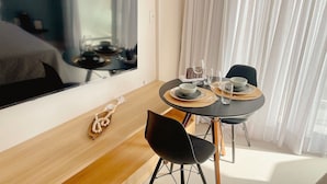 A dining area with a round table, black chairs, and a view of a cityscape through a window. - Aquamaris Luxo - by Almare (João Pessoa)