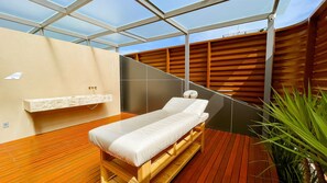 Une salle de spa moderne avec un plancher en bois, une table de massage, un mur à lattes de bois et un plafond en verre.