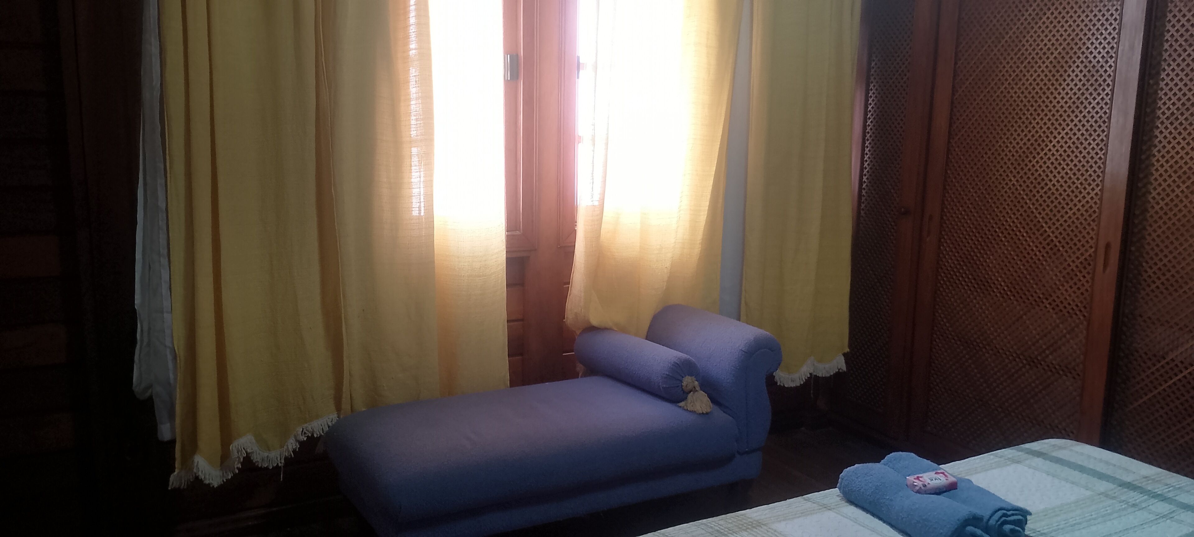 Una habitación con un sofá azul, una cama con una manta azul y cortinas amarillas.