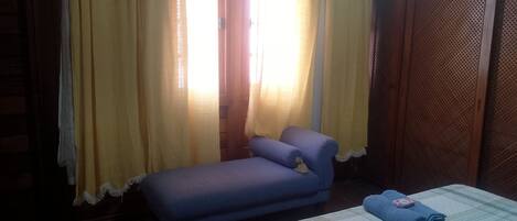 Una habitación con un sofá azul, una cama con una manta azul y cortinas amarillas.