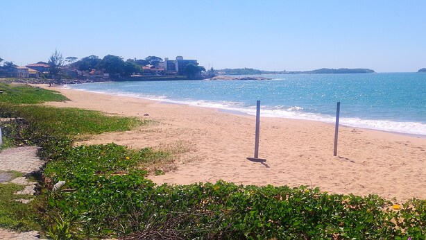 Ein Strand mit freiem Blick auf den Ozean, einem sandigen Ufer und einigen Gebäuden im Hintergrund.