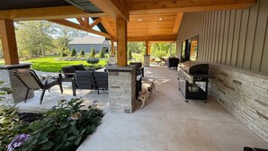 Un patio exterior con pilares de piedra, una parrilla y asientos.