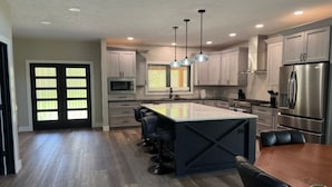 Una cocina moderna con una isla central, taburetes de bar, electrodomésticos de acero inoxidable e iluminación colgante.