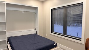 Un dormitorio con cama, estanterías empotradas, una ventana con persianas y piso alfombrado.