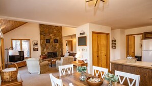A cozy living room with a fireplace, a dining area with a wooden table and chairs, and a kitchen with a refrigerator. - Private Pagosa Springs Retreat with Views, Hot Tub and Game Room (Pagosa Springs)