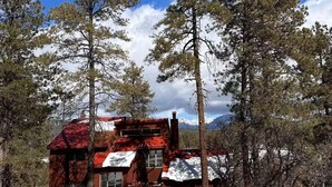 A rustic cabin with a red roof, surrounded by tall pine trees and a snowy landscape. - Private Pagosa Springs Retreat with Views, Hot Tub and Game Room (Pagosa Springs)