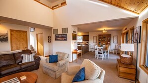 A spacious living area with a sofa, armchairs, and a dining table. There is a kitchen in the background with wooden cabinets and a hanging light fixture. - Private Pagosa Springs Retreat with Views, Hot Tub and Game Room (Pagosa Springs)