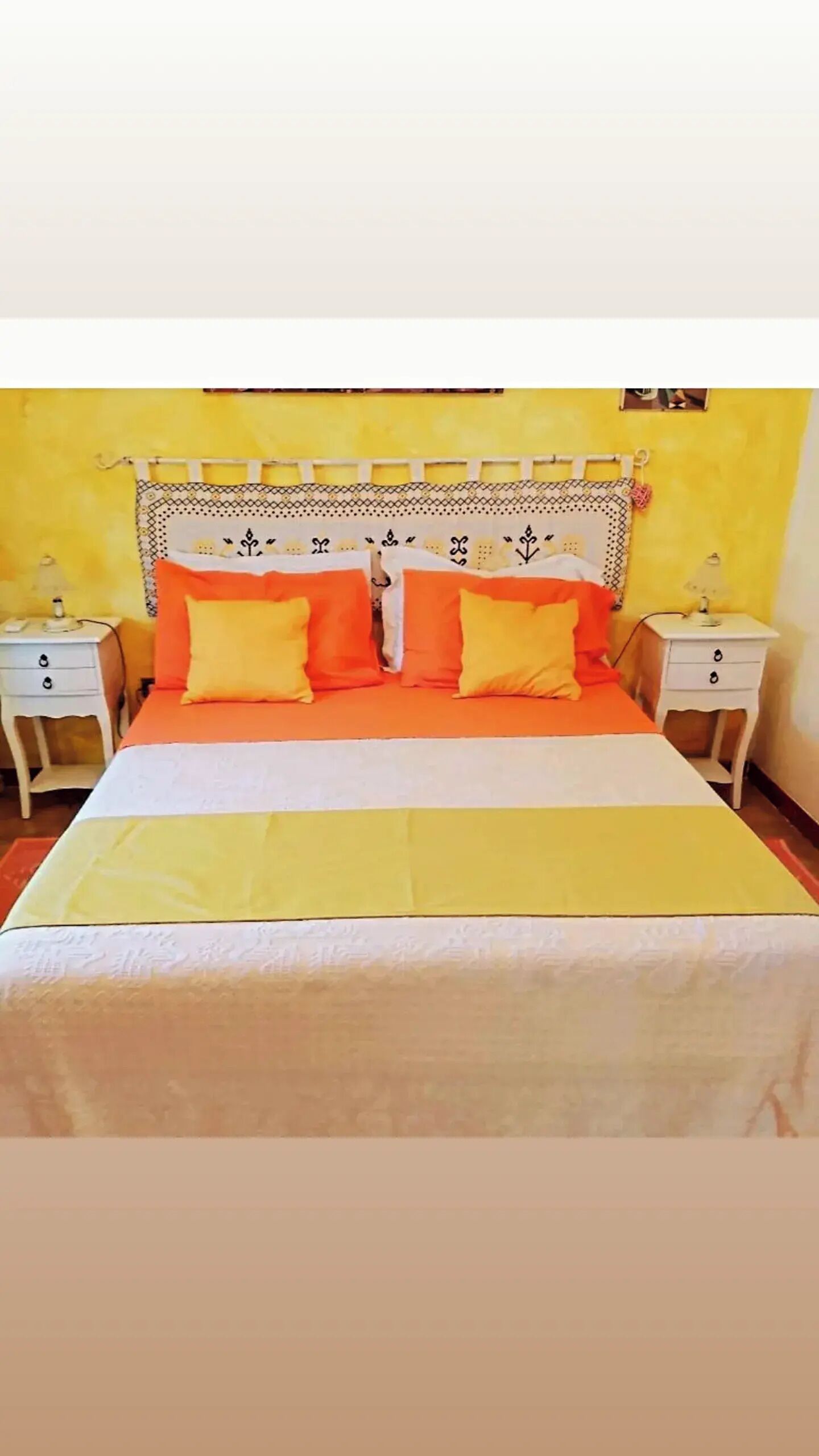 A bed with a white and orange bedspread, two white nightstands, and a yellow wall.