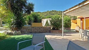 An outdoor patio with a table and chairs, surrounded by greenery and a yellow building. - Bed and breakfast il rosmarino  (Bosa)