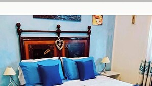 A bedroom with a bed, nightstands, a lamp, a blue and white bedspread, and a blue rug. - Bed and breakfast il rosmarino  (Bosa)