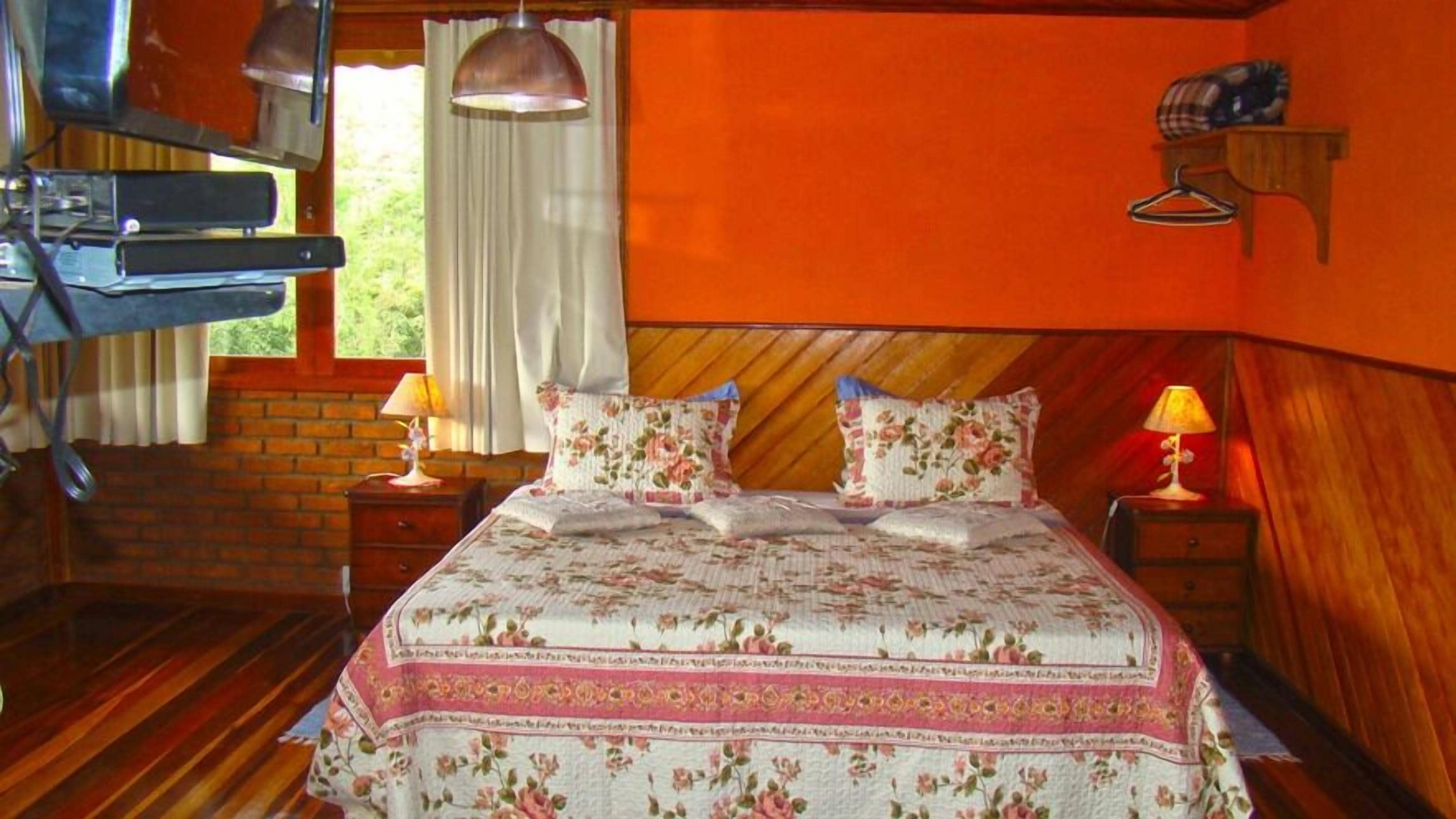 A bedroom with a wooden headboard, a bed with floral bedding, a nightstand with a lamp, and a window with curtains.