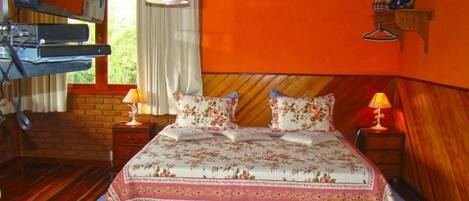 A bedroom with a wooden headboard, a bed with floral bedding, a nightstand with a lamp, and a window with curtains.