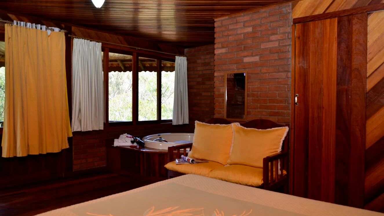 A room with a bed, a wooden bench, a small table with a sink, and a brick wall.