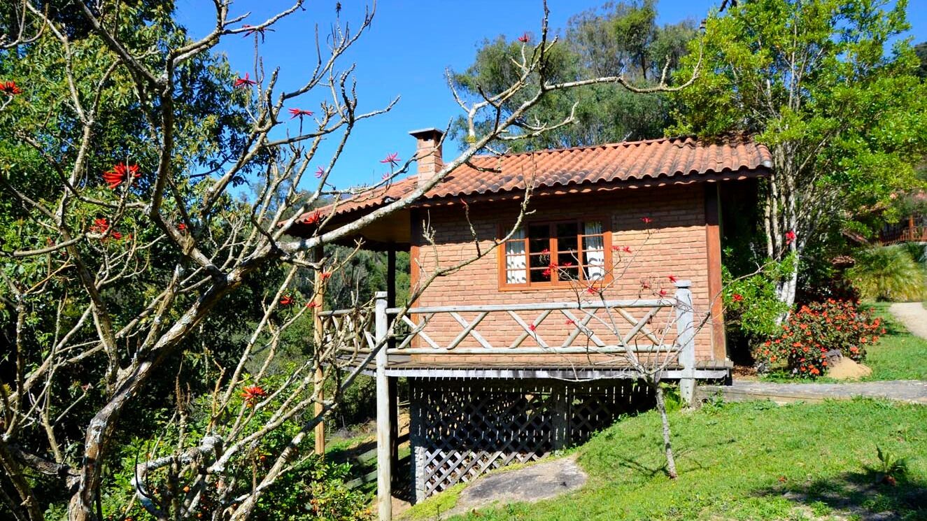 A rustic wooden house with a tiled roof, a wooden porch, and a garden with flowering plants.