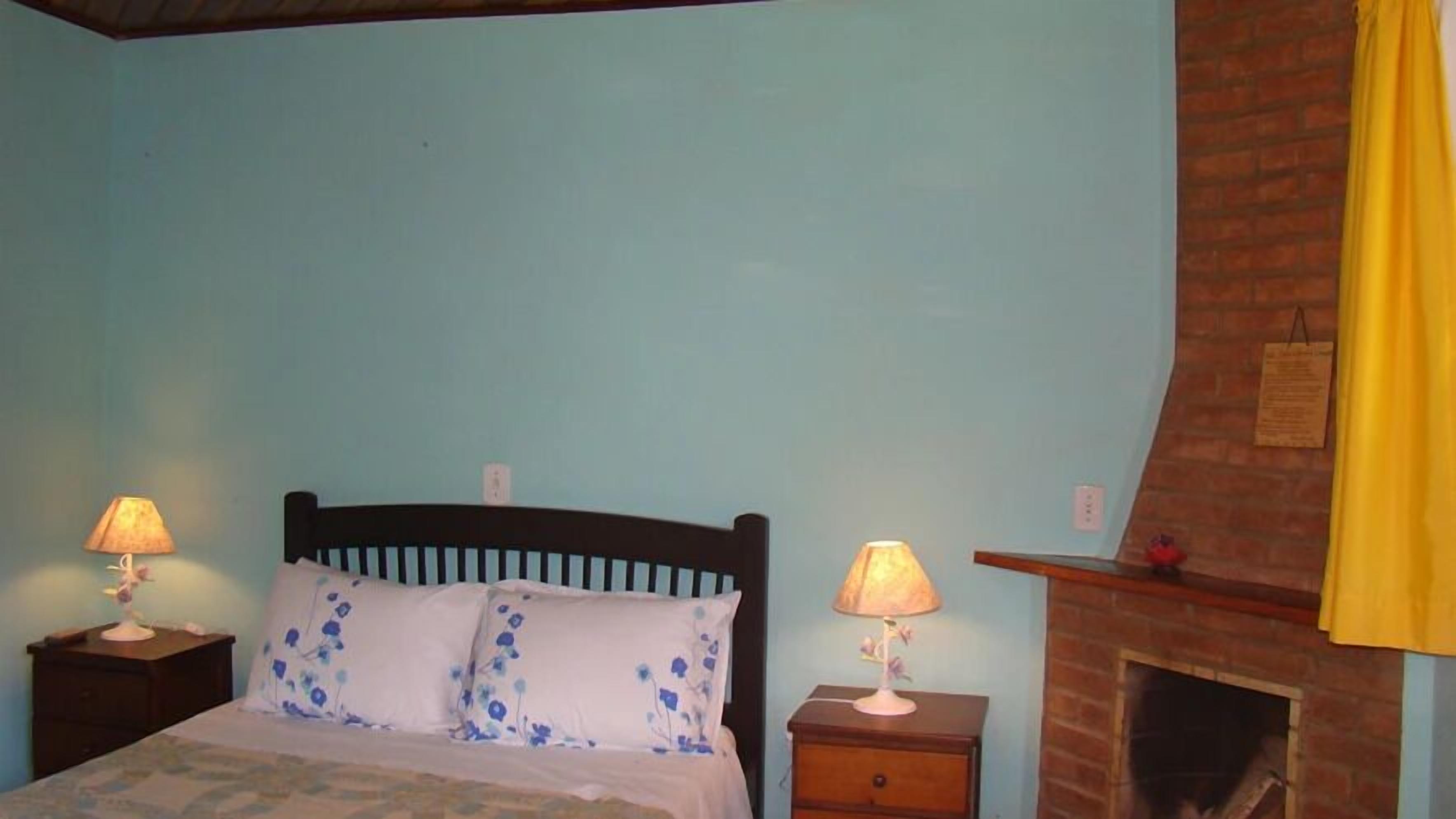 A bedroom with a bed, two bedside tables, a nightstand, a fireplace, and a wall-mounted shelf.