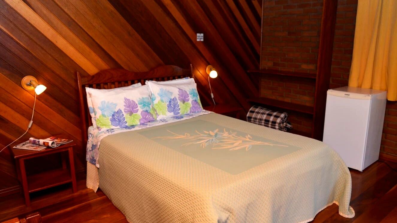 A cozy room with a bed, a nightstand, a lamp, and a small refrigerator.