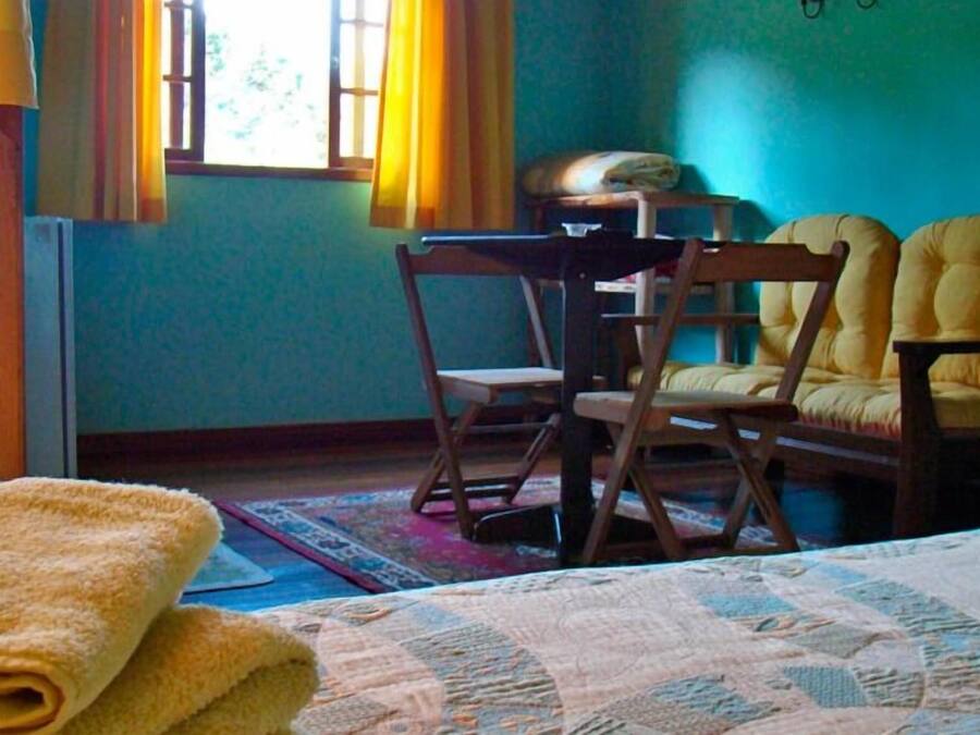 A room with a bed, two yellow armchairs, a wooden table, and a window with curtains.