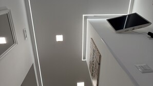 A modern, minimalist room with a white ceiling, recessed lighting, and a flat-screen TV on a white console.