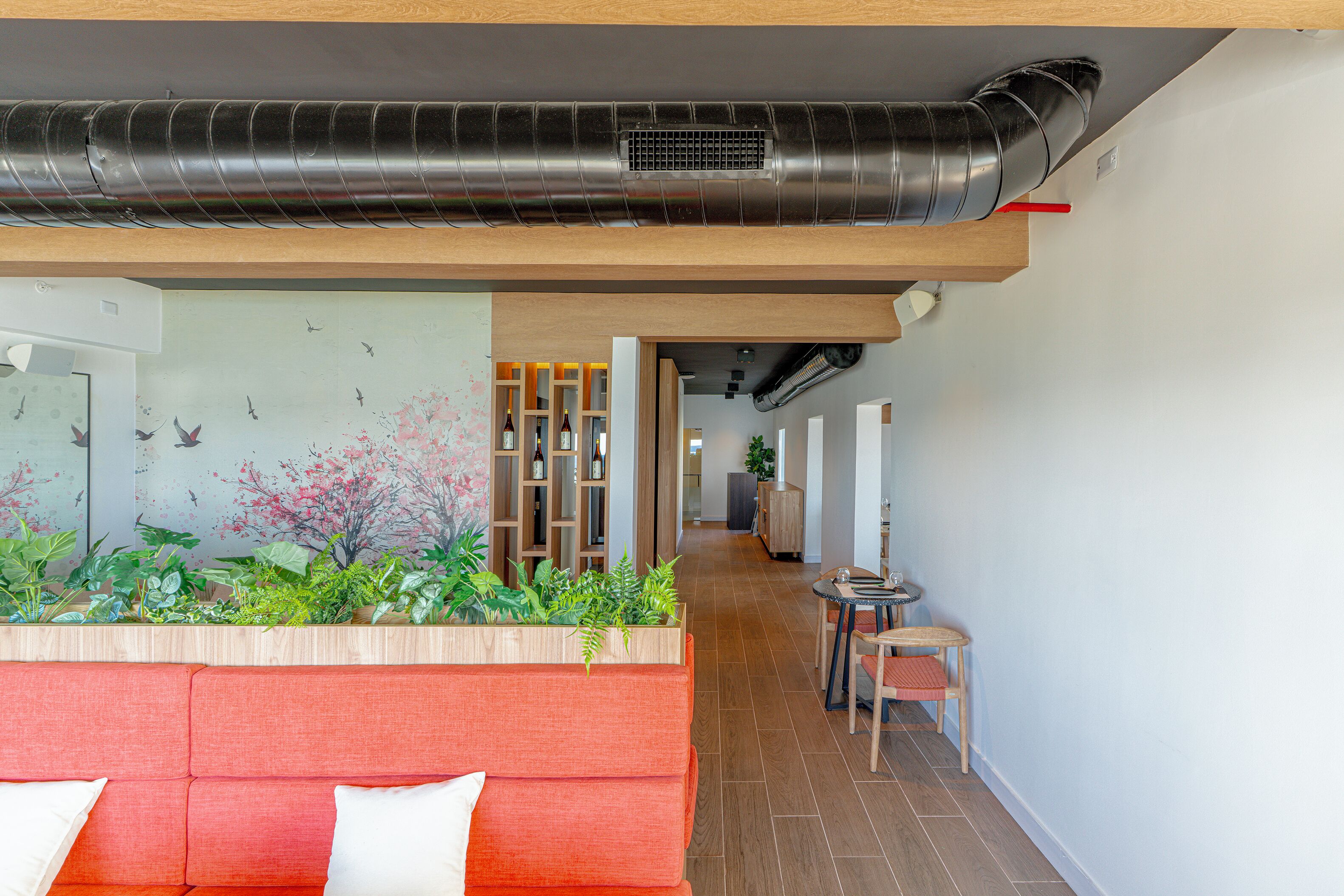 A modern interior with a red sofa, a wooden bench, a plant wall, and a hallway leading to a dining area.
